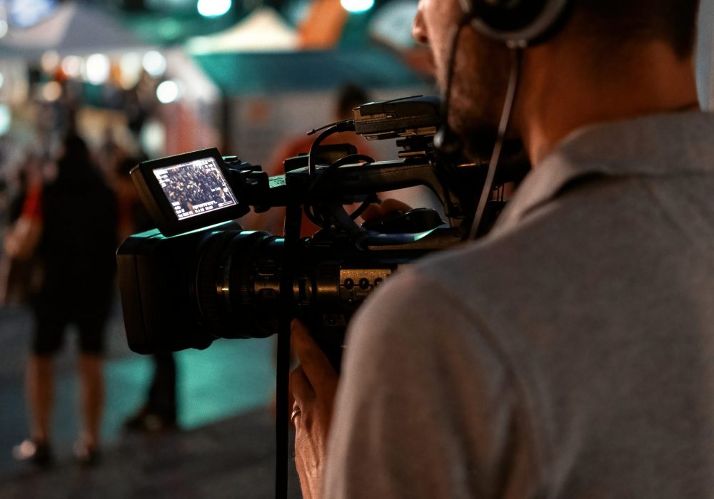 Professional cameraman recording poeple watching football in a public place at night